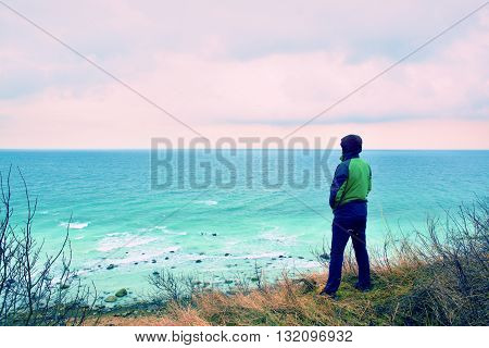 Man In Green Windcheater Stand On Cliff Above Bay And Looki At Sea Far Horizon.
