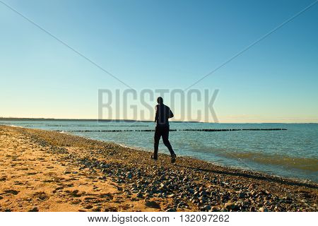 Tall Man In Dark Sportswer Running And Exercising On Stony Beach At Breakwater.