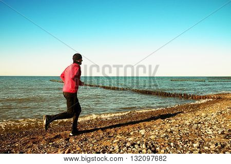 Tall Man In Dark Sportswer Running And Exercising On Stony Beach At Breakwater.