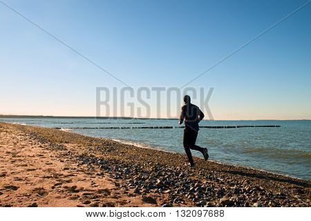 Tall Man In Dark Sportswer Running And Exercising On Stony Beach At Breakwater.