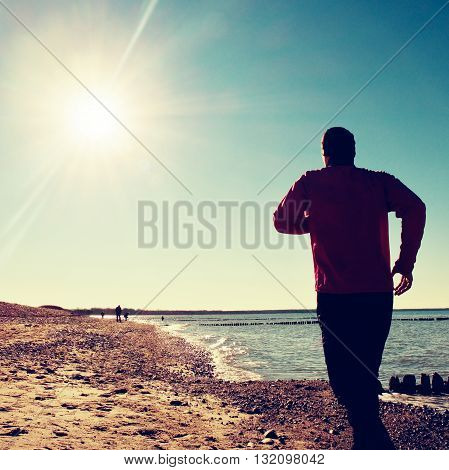Tall Man In Dark Sportswer Running And Exercising On Stony Beach At Breakwater.