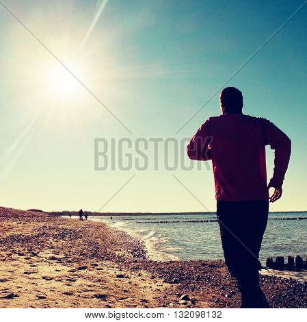 Tall Man In Dark Sportswer Running And Exercising On Stony Beach At Breakwater.