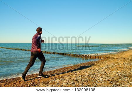 Tall Man In Dark Sportswer Running And Exercising On Stony Beach At Breakwater.