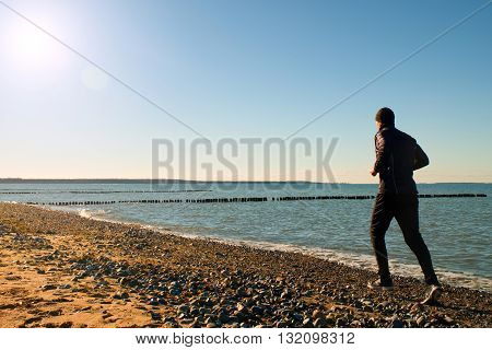 Tall Man In Dark Sportswer Running And Exercising On Stony Beach At Breakwater.
