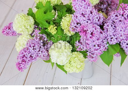 A tender bouquet of lilac and buldenezh, decorative form of Viburnum, in the form of a snow globe on a white wooden table in a silver vase