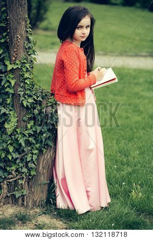 Girl In Dress With Notebook And Pen Near Tree