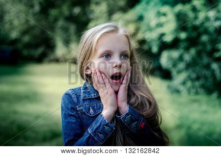 Surprised cute little blond girl at summer field.