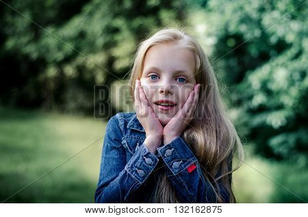 Surprised cute little blond girl at summer field.