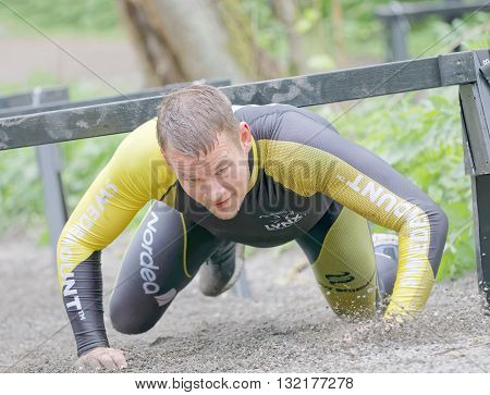 STOCKHOLM SWEDEN - MAY 14 2016: Smiling struggling man crawling under bars in the obstacle race Tough Viking Event in Sweden May 14 2016