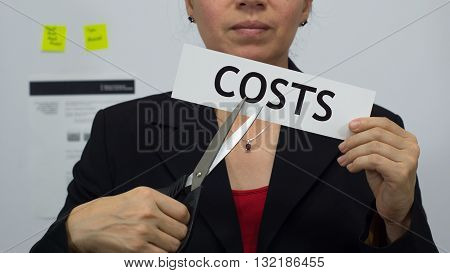 Female office worker or business woman cuts a piece of paper with the word costs on it as a cost reduction business concept.
