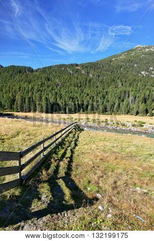 Scenic farm fields blocked bythe wooden fence. Shadow of the low fence beautifully lie on the grass. Alpine Valley in Austria. National Park Krimml 