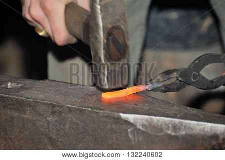 Blacksmith working metal with hammer on the anvil in the forge