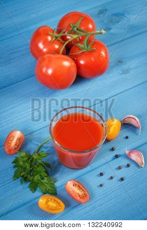 Glass of fresh tomato juice and ripe vegetable on blue board healthy nutrition