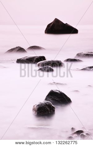 Romantic Morning At Sea. Big Boulders Sticking Out From Smooth Water Level. Pink Horozon With First