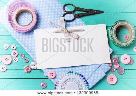 Sewing thread - buttons scissors fabric and empty tag on turquoise wooden background. Selective focus. Scrapbboking. Flat lay. Place for text. Toned image.