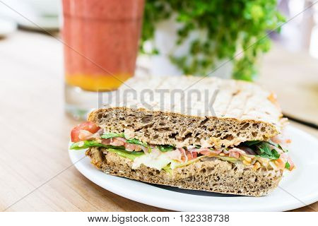 Sandwich with ham, tomato, rucola und salad serviert with smoothie on wooden table.