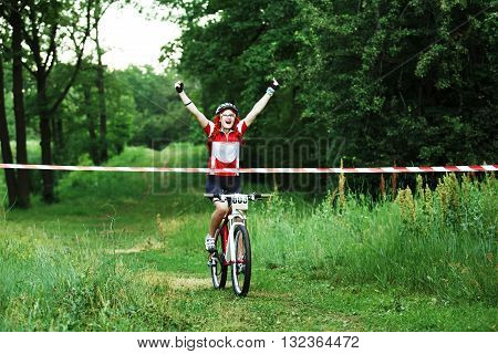 Winner of mtb race. Victory moment. Young female cyclist in protective helmet crossing the finish line breaking the tape. Victory triumph in sportive competition, wins the cycling race. Bicycle sport.