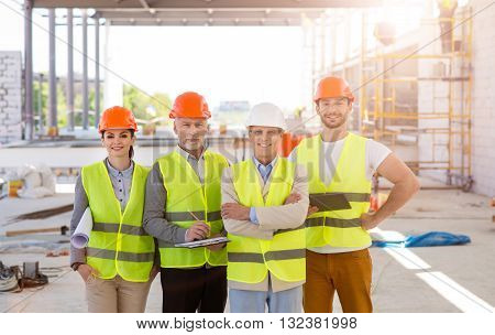 Engineering. A confident group of engineers standing together and looking at a camera with construction works and builders on a background