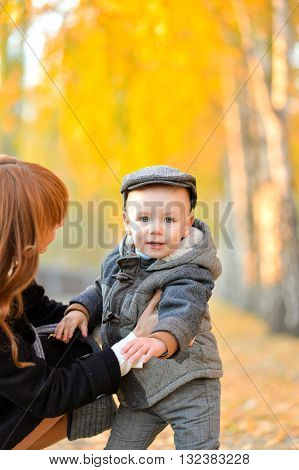 Heppy mother stends with a cheerful toddler in the park in autumn.
