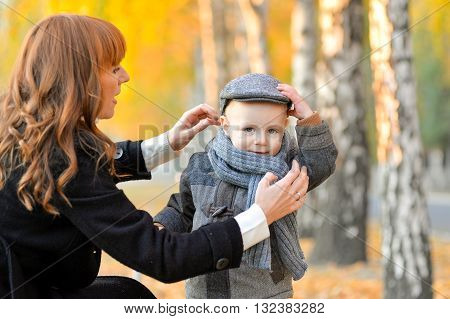 Heppy mother stends with a cheerful toddler in the park in autumn.
