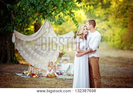 Beautiful pregnant woman with her husband and young daughter in green garden