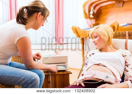 Midwife exanimating belly of pregnant woman with CTG scanning in practice