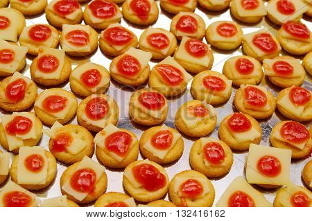 Tray of biscuits with cheee and red topping, lined up on metal surface.