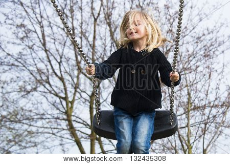 Little child blond girl having fun on a swing outdoor. Summer playground. Girl swinging high