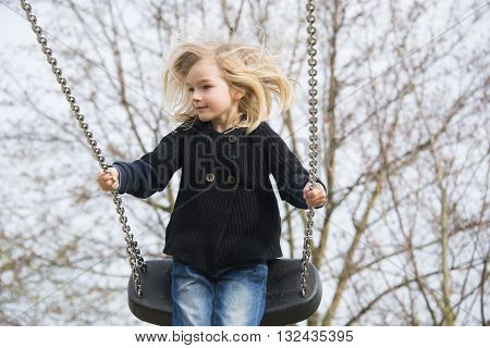 Little child blond girl having fun on a swing outdoor. Summer playground. Girl swinging high