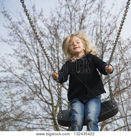 Little child blond girl having fun on a swing outdoor. Summer playground. Girl swinging high