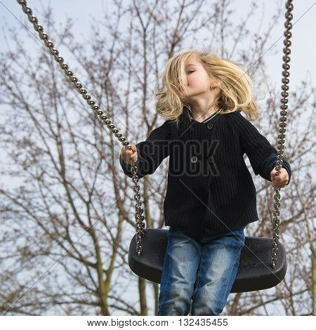 Little child blond girl having fun on a swing outdoor. Summer playground. Girl swinging high