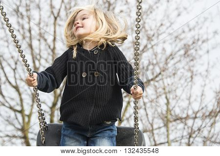 Little child blond girl having fun on a swing outdoor. Summer playground. Girl swinging high