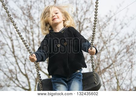 Little child blond girl having fun on a swing outdoor. Summer playground. Girl swinging high