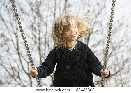 Little child blond girl having fun on a swing outdoor. Summer playground. Girl swinging high