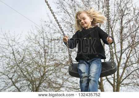 Little child blond girl having fun on a swing outdoor. Summer playground. Girl swinging high
