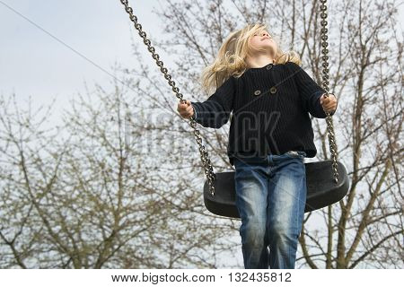 Little child blond girl having fun on a swing outdoor. Summer playground. Girl swinging high
