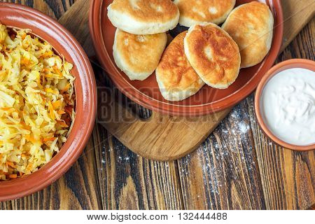 Traditional homemade pies with cabbage and sauerkraut on the plate on wooden board. Savory stuffed patties also known as pastel, pate or piroshki. Fried russian pastry pirozhki on wooden background.