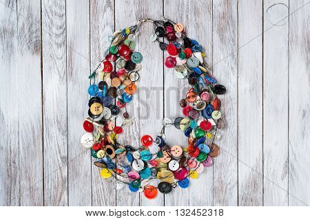 Handmade bright colored jewelry made of plastic buttons on the white wooden background.