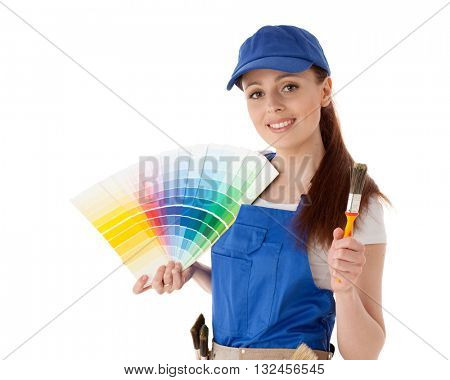 Young woman in  coverall with a color guide and paintbrushes on a white background.