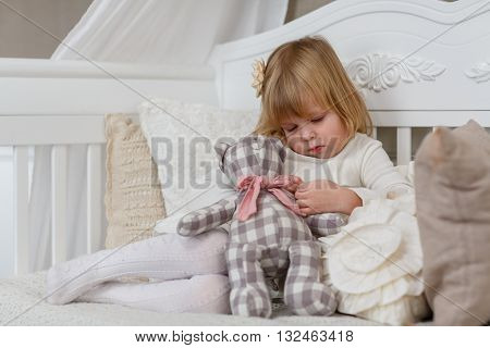Sad pretty girl with toy bear sits on a sofa in the room.