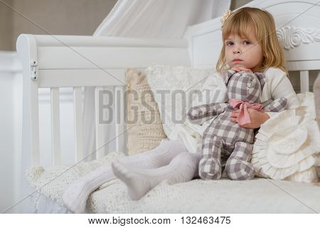 Sad pretty girl with toy bear sits on a sofa in the room.