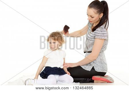 Young mother brushing hair of the small daughter on a white background.
