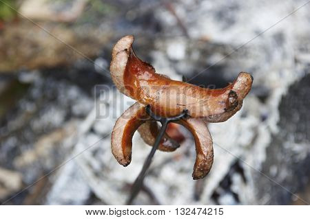 Sausage on a stick over the fire. Preparing sausages on camp fire
