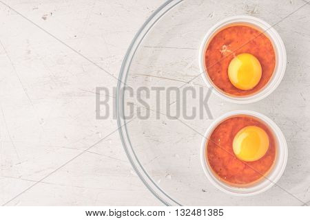 Raw eggs with tomatoes in the ramekins on the white wooden table top view