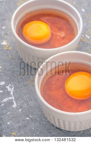 Raw eggs with tomatoes in the ramekins on the stone table vertical
