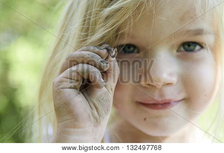 Four year old child blond girl holding a worm in the garden