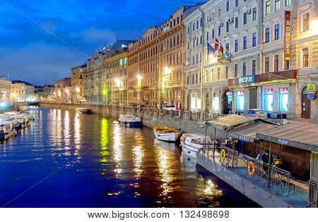 SAINT-PETERSBURG, RUSSIA - APRIL 21, 2016: Man stand on the pier near excursion boats on the Moika River close to The Nevsky Avenue and The Green Bridge. On the background is The Pevchesky Bridge. Night view.