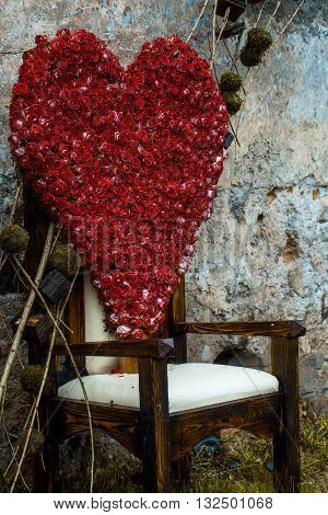 Floral arrangement with red rose flowers in shape of heart on chair outdoor on stony wall background