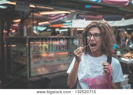 Street food in Kuala Lumpur Malaysia. Traveling woman eating voraciously chopped fruit from local market vendor. Toned image instagram style.