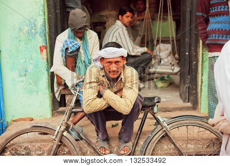 VARANASI, INDIA - JAN 1, 2013: Happy poor man sitting with his cycle on the street of poor area of indian city on January 1, 2013. Varanasi urban agglomeration had a population of 1435113